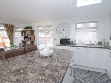 A kitchen and dining area with a large clock on the wall a microwave and a bookshelf at Swifts Reach Lodge Kirkstone 10 Limefitt Park near Windermere