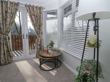 A corner of a room with glass double doors floral curtains nested wooden tables and a floor lamp with plants at Swifts Reach Lodge Kirkstone 10 Limefitt Park near Windermere