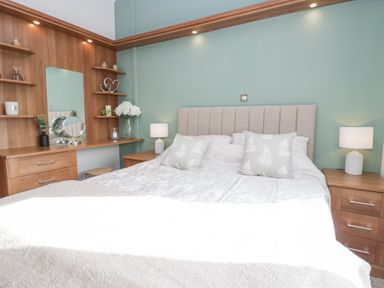 A bedroom with a bed between two bedside tables with lamps and a wooden dressing table with shelves on a green wall at Swifts Reach Lodge Kirkstone 10 Limefitt Park near Windermere