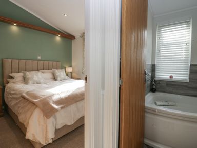 A bedroom with a bed and pillows next to a bathroom with a bathtub and a window with blinds at Swifts Reach Lodge Kirkstone 10 Limefitt Park near Windermere