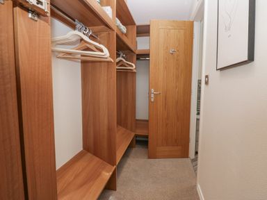 A walk-in closet with wooden shelves hangers and an open wooden door at Swifts Reach Lodge Kirkstone 10 Limefitt Park near Windermere