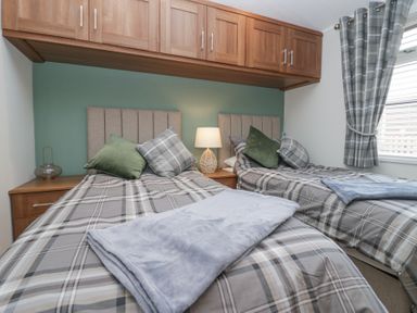 A bedroom with two single beds green and gray pillows wooden overhead cabinets and gray plaid curtains at Swifts Reach Lodge Kirkstone 10 Limefitt Park near Windermere