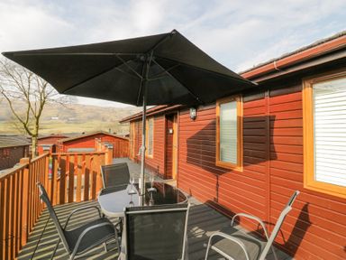 A wooden deck with a table, chairs, and a black umbrella at Swifts Reach Lodge in Kirkstone 10, Limefitt Park near Windermere
