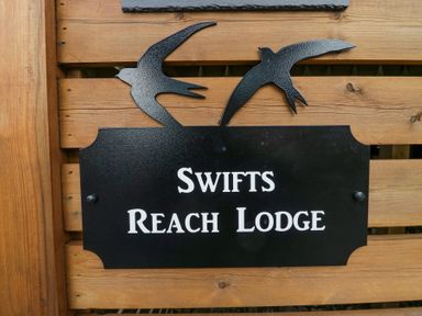 A black sign with two bird shapes and the text Swifts Reach Lodge on a wooden surface at Swifts Reach Lodge Kirkstone 10 Limefitt Park near Windermere