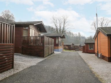 A pathway between wooden lodges with leafless trees and hills in the background at Swifts Reach Lodge Kirkstone 10 Limefitt Park near Windermere