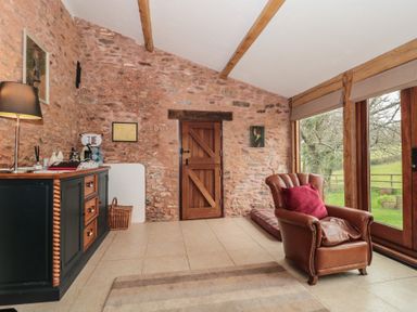 A room with a leather armchair a wooden sideboard and a wooden door with stone walls and large windows showing a garden at The Barn in Spaxton