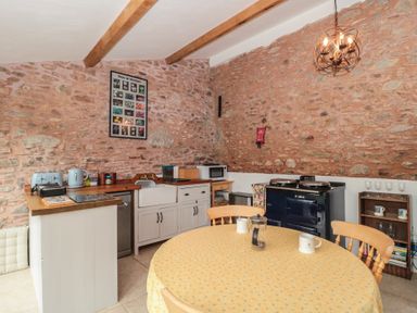 A kitchen with stone walls a round table with chairs and a stove at The Barn in Spaxton