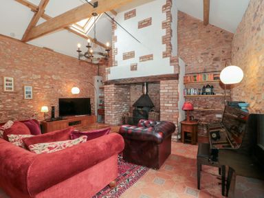A living room with a red sofa a leather armchair a piano a TV and a fireplace at The Barn in Spaxton