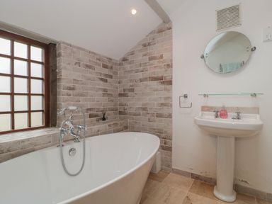 A bathroom with a freestanding bathtub a sink with mirror and tiled walls at The Barn in Spaxton