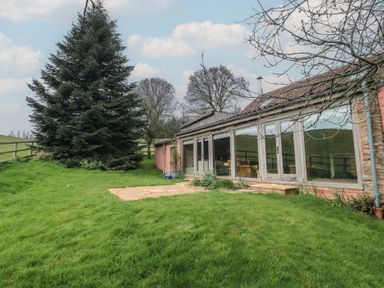 A grassy yard with a large tree and a building with large windows and a tiled roof at The Barn in Spaxton