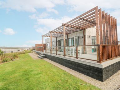 A wooden deck with a pergola and outdoor dining furniture next to a grassy area at Hepworth in Portreath