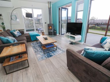 A living room with brown sofas and blue cushions a wooden coffee table wood burner and a television at Hepworth in Portreath
