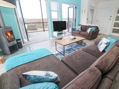 A living room with two brown sofas pillows a wooden coffee table a television a fireplace and an open door to a deck at Hepworth in Portreath