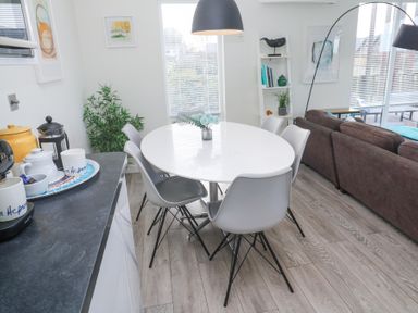 A dining area with a round white table and six grey chairs next to a brown sofa and a black countertop in Hepworth Portreath
