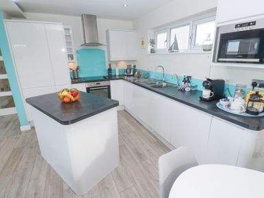 A kitchen with white cabinets black countertops a kitchen island with a fruit basket and appliances at Hepworth in Portreath