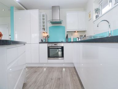 A kitchen with white cabinets black countertops a stainless steel oven and a blue backsplash at Hepworth in Portreath