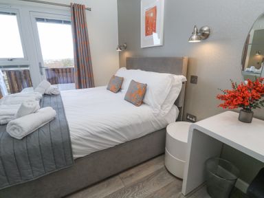 A bedroom with a bed with pillows and folded towels next to a window and a table with flowers at Hepworth in Portreath