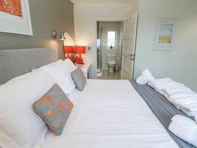 A bedroom with a bed with white and grey bedding two pillows with orange flowers a door leading to a bathroom with a toilet and shower at Hepworth in Portreath