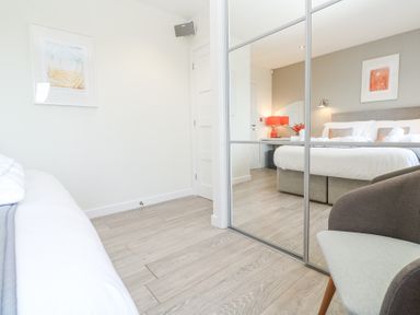 A bedroom with a large bed a bedside table with a lamp and flowers a chair and a mirrored wardrobe at Hepworth in Portreath