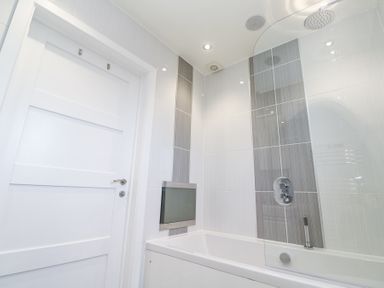A bathroom with a white door a bathtub a glass shower screen and tiled walls