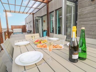 An outdoor dining table with plates glasses pastries fruit and bottles on a terrace with wooden walls at Hepworth in Portreath