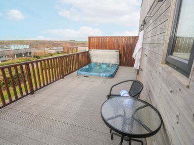 An outdoor balcony with a hot tub table and chair and wooden railing at Hepworth Portreath