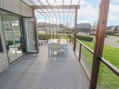 A wooden deck with a dining table and chairs under a pergola next to a house at Hepworth in Portreath