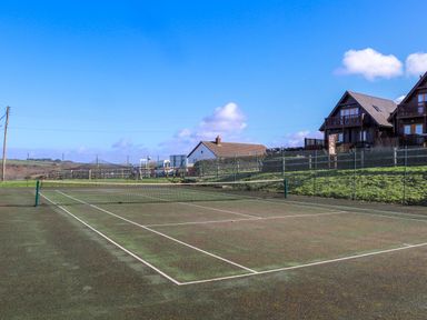 An outdoor tennis court with a net and fencing surrounded by houses and grassy hills at Hepworth Portreath