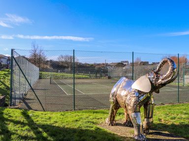 An outdoor tennis court with a metal elephant sculpture on grass in the foreground at Hepworth in Portreath
