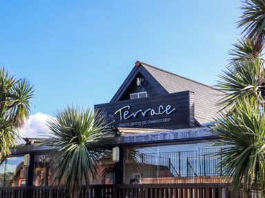 An exterior view of a building with a sign that reads The Terrace Bistro dining at Gwelan Mor with palm trees around Hepworth Portreath