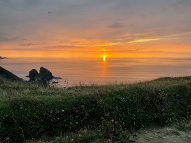 A coastal landscape with rocky formations in the ocean at sunset in Portreath