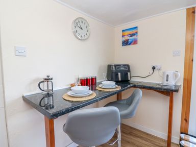 A kitchen corner with a black countertop table set for two with plates and glasses a clock on the wall and kitchen appliances at Shed Your Blues in Brilley near Kington