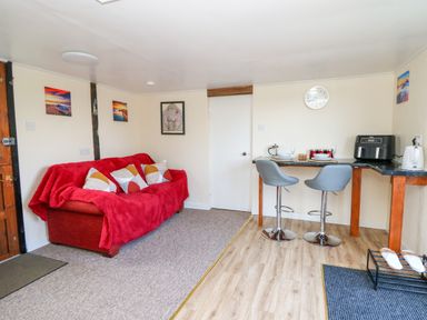 A small living area with a red sofa and cushions next to a breakfast bar with two stools and kitchen appliances at Shed Your Blues in Brilley near Kington