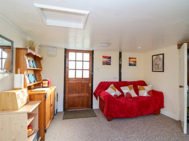 A living room with a wooden door a red covered sofa and wooden cabinets at Shed Your Blues in Brilley near Kington