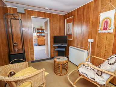 A small sitting room with wicker chairs a small round table a television and wood panelled walls at Shed Your Blues in Brilley near Kington