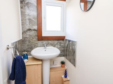 A small bathroom with a pedestal sink a window above and a wooden cabinet next to it at Shed Your Blues Brilley near Kington