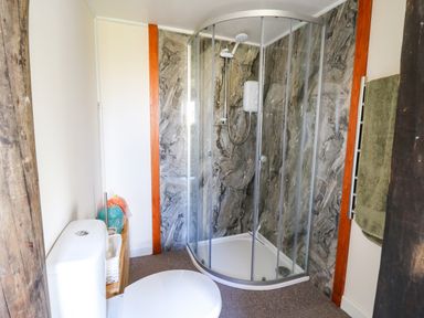 A bathroom with a toilet a corner shower with glass doors and stone effect walls at Shed Your Blues in Brilley near Kington