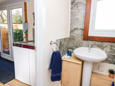 A small bathroom with a sink and a towel hanging on a ring next to a kitchen area with a stove and glass doors at Shed Your Blues Brilley near Kington