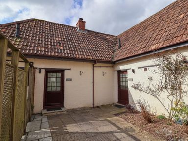 An outdoor courtyard with two doors labeled Garden Cottage and Meadow Cottage with tiled roofs and some plants at Garden Cottage in Upottery