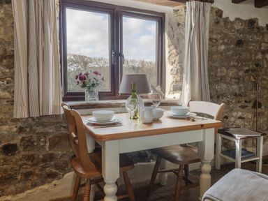 A dining table set for two with chairs by a window in a stone walled room at Garden Cottage in Upottery