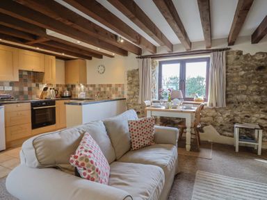 A kitchen and dining area with a sofa and wooden beams on the ceiling at Garden Cottage in Upottery