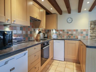 A kitchen with wooden cabinets countertop dishwasher and microwave at Garden Cottage in Upottery