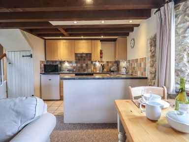 A kitchen with wooden cabinets and tiled backsplash next to a wooden dining table with dishes at Garden Cottage in Upottery