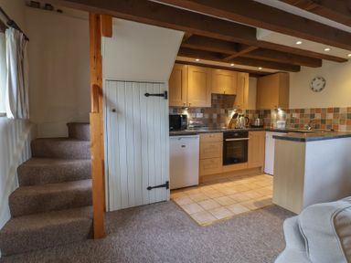 A kitchen area with wooden cabinets and tiled floor next to carpeted stairs at Garden Cottage in Upottery