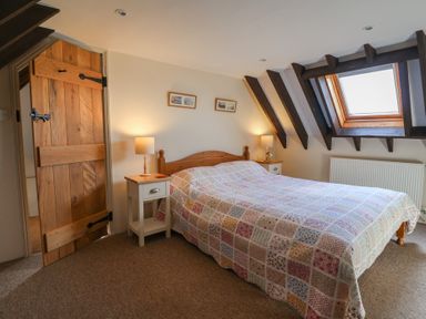 A bedroom with a wooden bed covered by a patchwork quilt two bedside tables with lamps a wooden door and a skylight window at Garden Cottage in Upottery