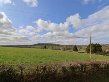 A green field with trees and hills under a blue sky with clouds at Garden Cottage in Upottery