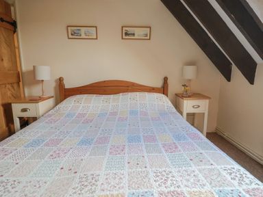 A bedroom with a wooden bed with a colorful patchwork quilt two nightstands with lamps and pictures on the wall at Garden Cottage in Upottery