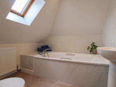A bathroom with a bathtub under a slanted ceiling window a sink and a radiator at Garden Cottage in Upottery