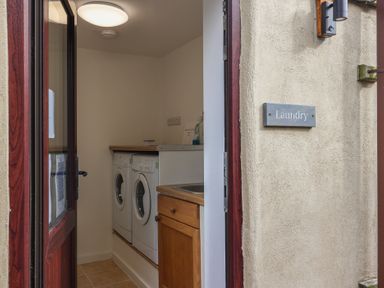 A laundry room with a washing machine a dryer a wooden cabinet and tiled floor at Garden Cottage in Upottery