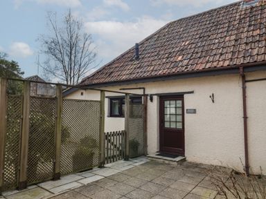 An exterior view of a cottage with tiled roof wooden lattice fencing and a paved patio at Garden Cottage in Upottery
